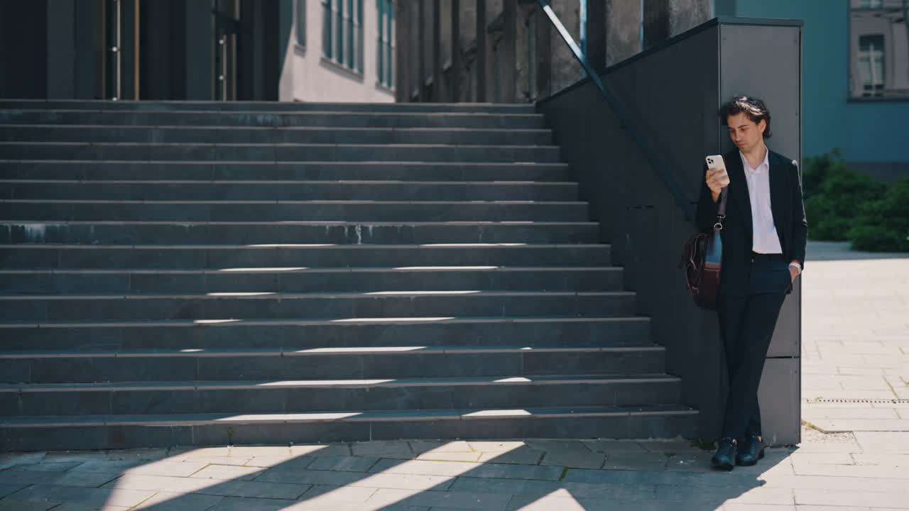 Young man in business casual attire using his smartphone outdoors near a modern building's stairs
