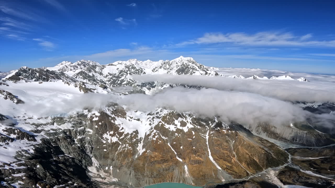 POV flying over the southern Alps of New Zealand, with lakes, clouds and snow covered mountains below