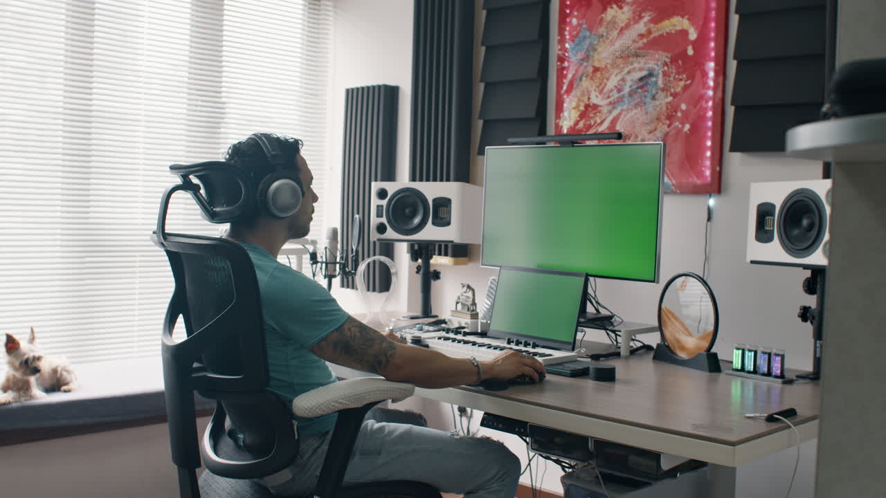Music producer uses headphones and mixing setup in bright home studio with green displays