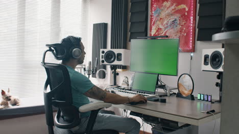 music producer uses headphones and mixing setup in bright home studio with green displays