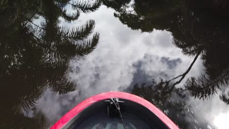 Traveling-with-a-boat-on-the-Tortuguero-Canal-,-looking-at-the-bow-and-the-clear-river-water-reflecting-the-cloudy-sky-and-the-trees