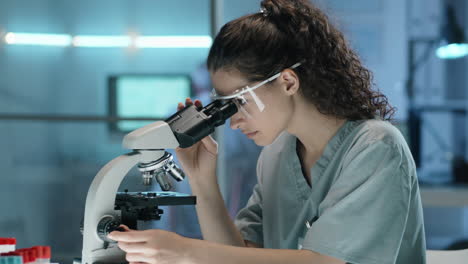 young female scientist using microscope and taking notes