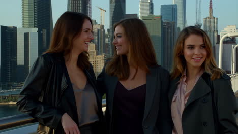 three women standing on a bridge with a city skyline background