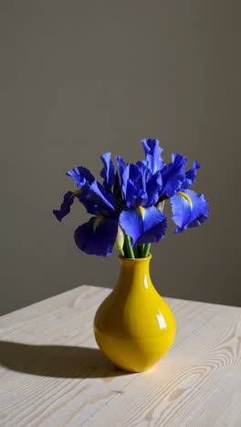 blue irises in a yellow vase on a wooden table