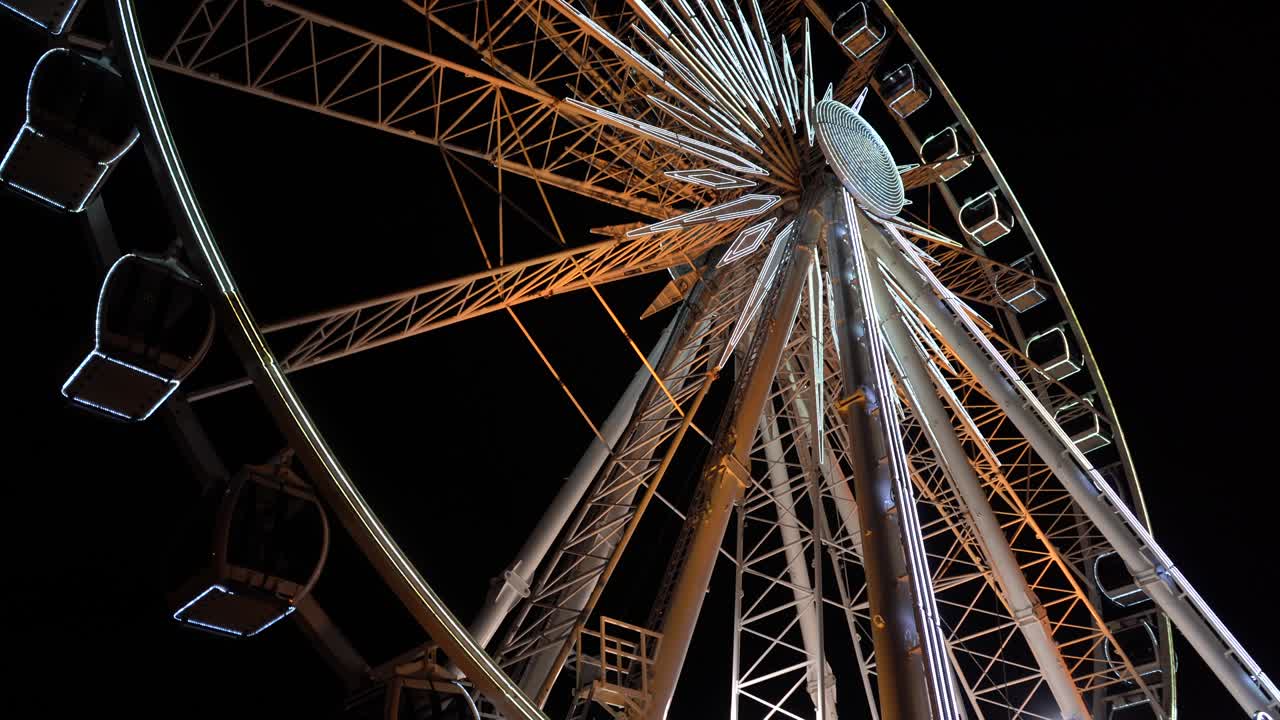 Ferris wheel. A ferris wheel rotates against the background of the night sky. Close-up of a Ferris wheel with night illumination. lluminated Ferris Wheel construction rotating against dark night sky background.