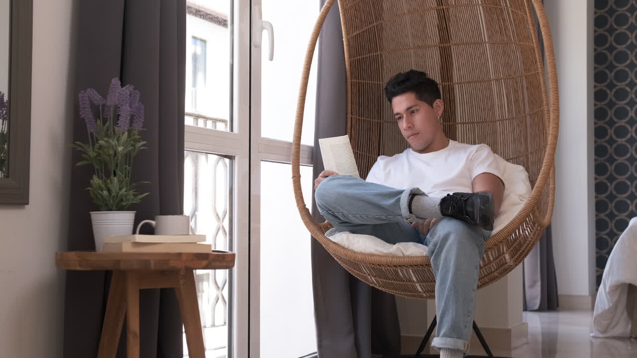 Portrait of young man reading a book while sitting in a comfortable chair at home.