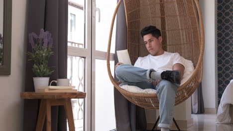 portrait of young man reading a book while sitting in a comfortable chair at home.