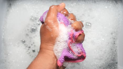 washing a purple and pink dishcloth in soapy water