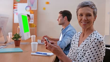 Casual-businesswoman-texting-while-her-colleagues-working-on-laptop-