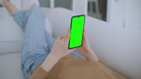 close-up shot of green screen template smartphone in female hands at home girl is watching content without touching gadget screen. modern technology and information concept.