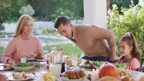 video of happy caucasian father, daughter and grandparents sitting down at outdoor dinner table