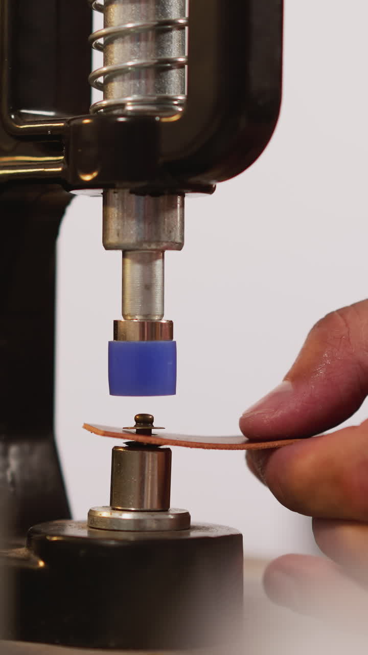 Master installs rivet into leather detail with machine tool in workshop closeup. Craftsman puts fastening on handmade accessory. Creative hobby