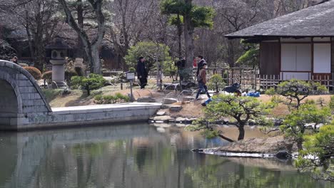 a peaceful garden scene featuring a stone path, traditional building, and reflective pond under a clear sky.