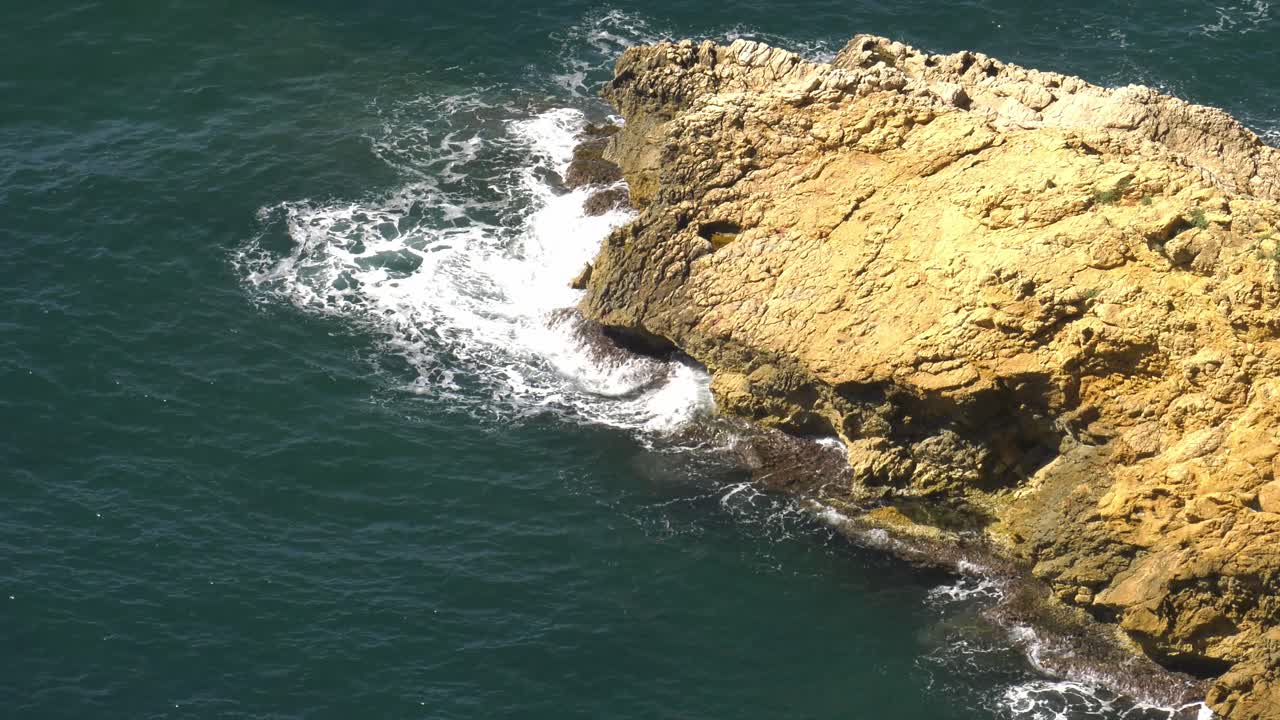 mar turquesa rompiendo en olas blancas contra un promontorio rocoso, vista de pájaro