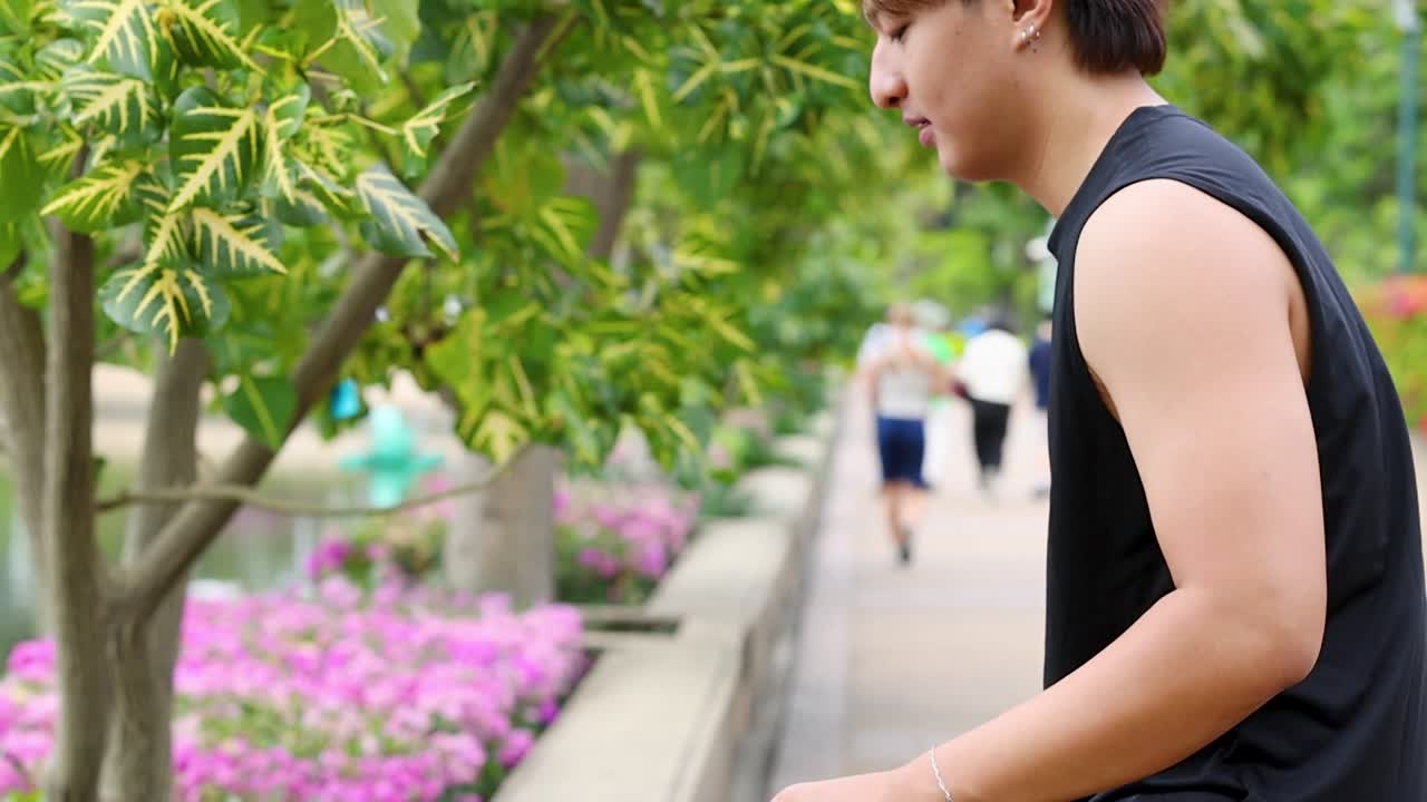 Một người đàn ông châu Á khỏe mạnh mặc áo ba lỗ màu đen đang tập các bài tập giãn cơ trong công viên