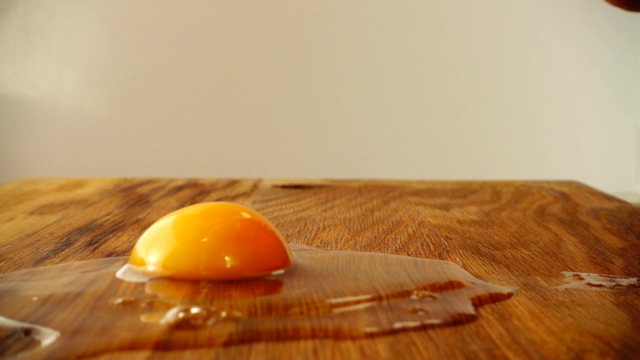 The cook breaks the egg on the cutting board. Slow motion.