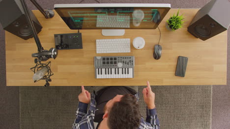 overhead view of male musician dancing at workstation with keyboard and microphone in studio