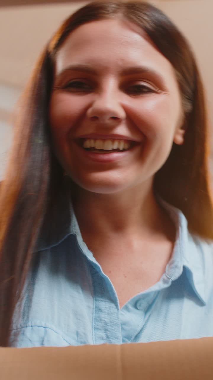 Felice giovane donna caucasica, acquirente, che disimballa il pacco di cartone ricevuto da un acquisto online.
