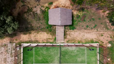 drone aerial view of an outdoor tennin or padle pitch with green, sandy ground, surrounded by stones and earth