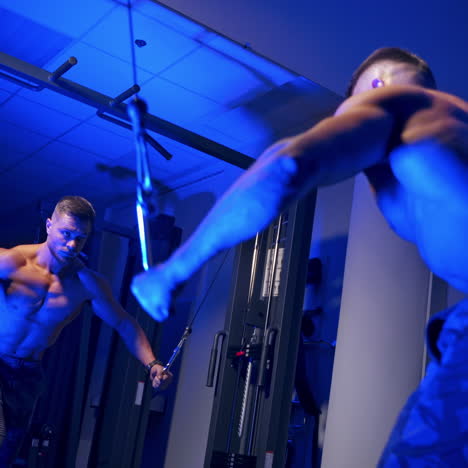 handsome bodybuilder doing workout pushing up excercise in gym in front of the mirror. blue light filter, naked torso. shirtless trainer. video from the side.