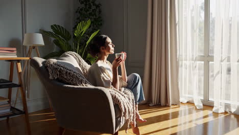 woman relaxing in an armchair with a cup in warm sunlight