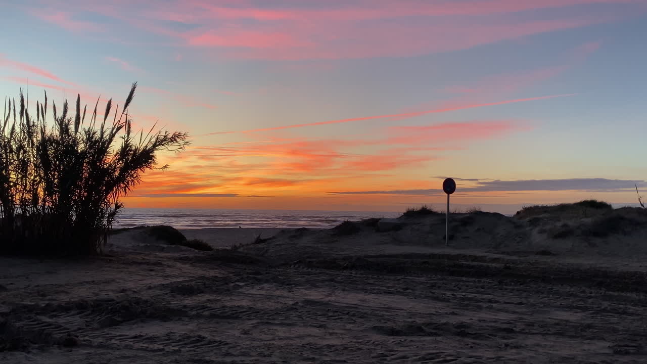 Doñana-færgen hviler ved lavvande på Sanlucar de Barrameda-kysten, mens flammende skyer maler himlen i livlige solnedgangsfarver.