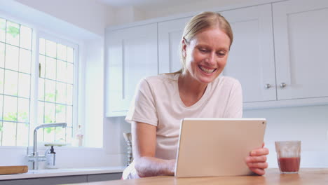 Mature-Woman-At-Home-In-Kitchen-Laughing-At-Show-Streaming-On-Digital-Tablet