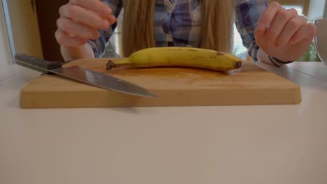 this is a 4k 60fps slow motion shot of a girl picking up a banana and utting it down on a cutting board