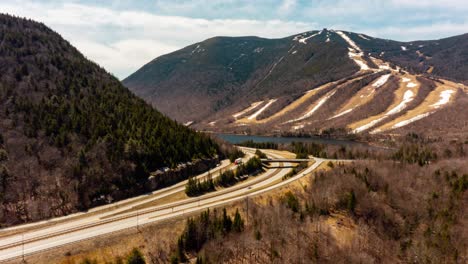 Busy-interstate-with-shipping-and-receiving-trucks-and-cars-in-mountains-with-alpine-lake-Drone-Aerial-time-lapse-hyper-lapse-4k-30p