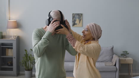 mujer árabe de mediana edad ayudando a un anciano feliz a usar gafas de realidad virtual en casa 2