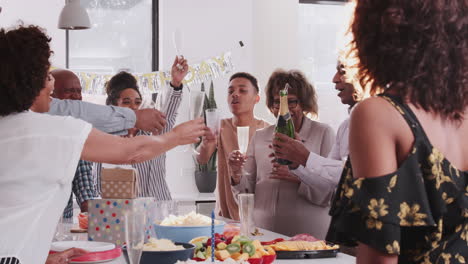 hombre negro de mediana edad abriendo y sirviendo champán en una celebración familiar, por encima del hombro