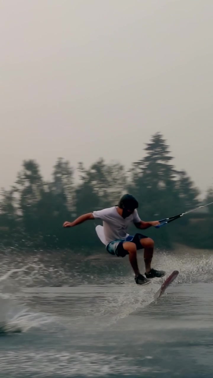 Vertical video: Cable pulling helmeted man riding wakeboard to left ramp, sliding popping for trick