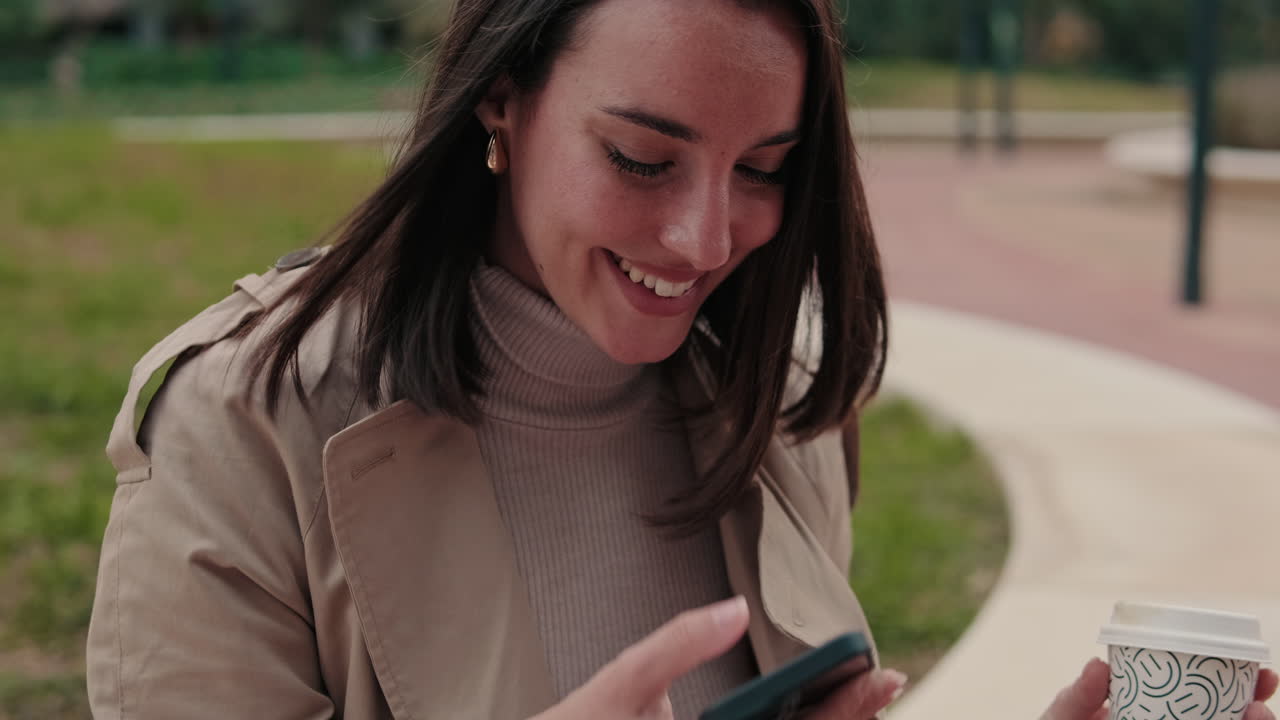 Giovane donna che sorride e usa lo smartphone all'aperto con un caffè