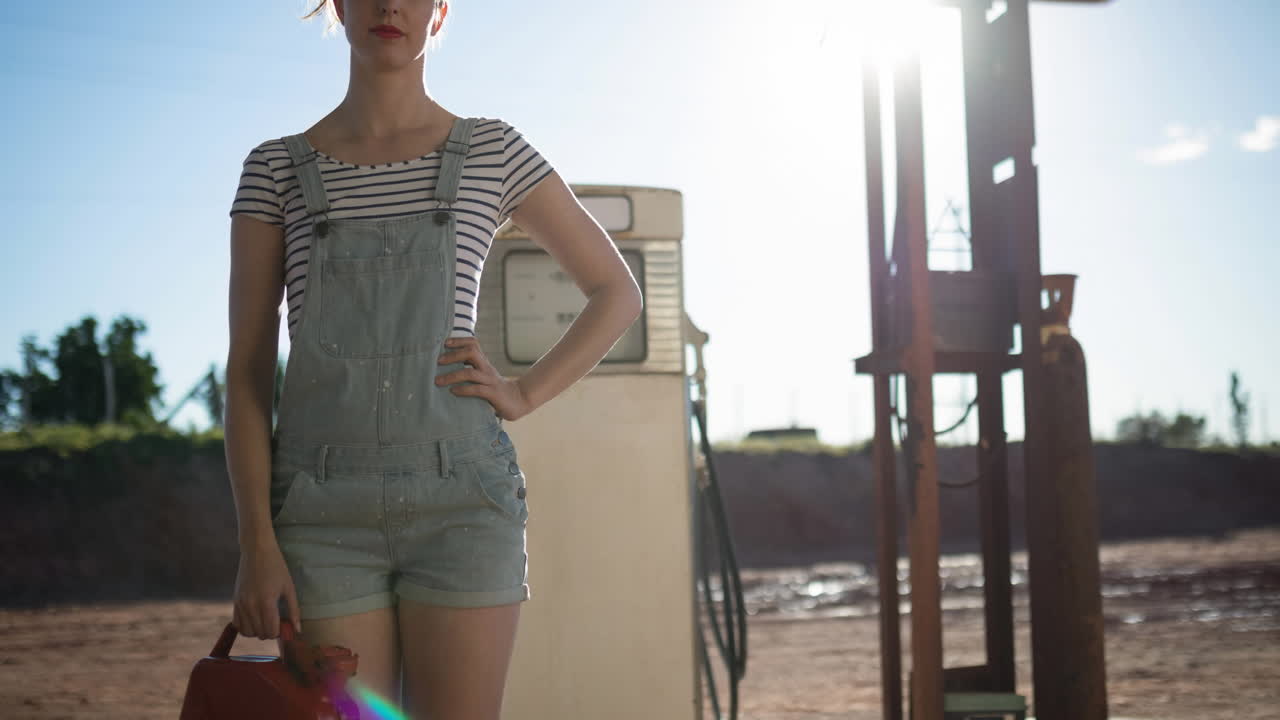 sección media de una mujer caucásica sosteniendo un depósito de combustible en una gasolinera soleada