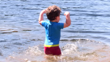 a small child is excited to splash in the water of a pond