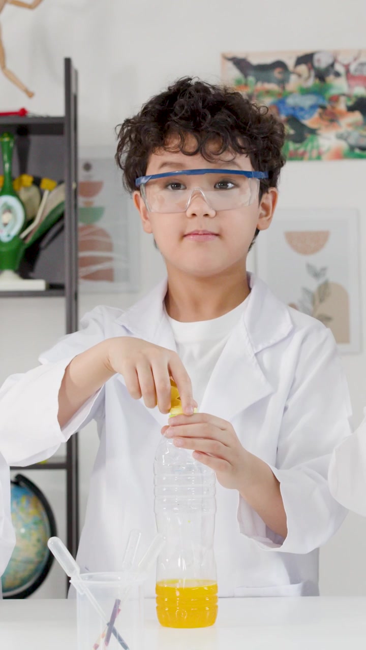 Anak laki-laki mengenakan jas lab memasang balon ke botol plastik selama pelajaran sains.