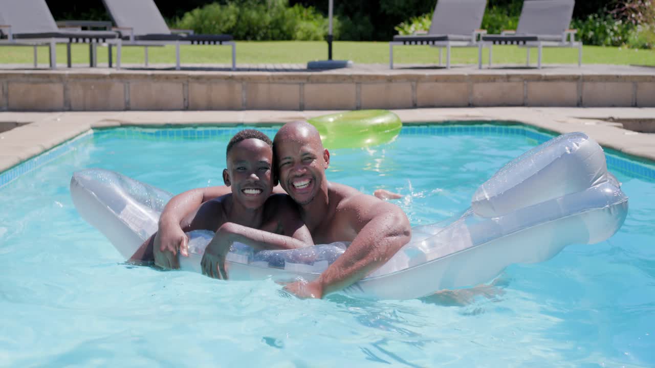African American father and son in swimwear on float at pool, father starting splash, helping drill
