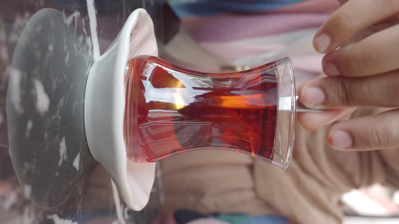 A hand stirring traditional Turkish tea in a glass