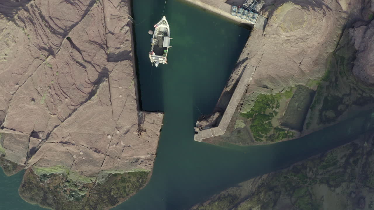 una vista aérea de arriba hacia abajo que se mueve sobre un pequeño puerto pesquero con un bote y algunas redes de creel, east lothian, escocia