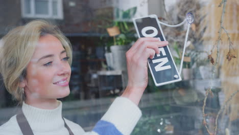 smiling female owner of small business turning round open sign in shop window