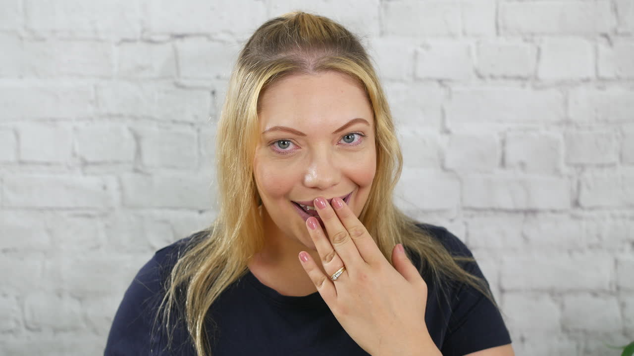 Uma mulher loira feliz, surpreendida e chocada, com a mão na boca, e envergonhada