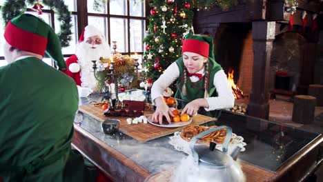 two elves playing at the table in decorated room for christmas. elves joking with eack other sitting next to santa