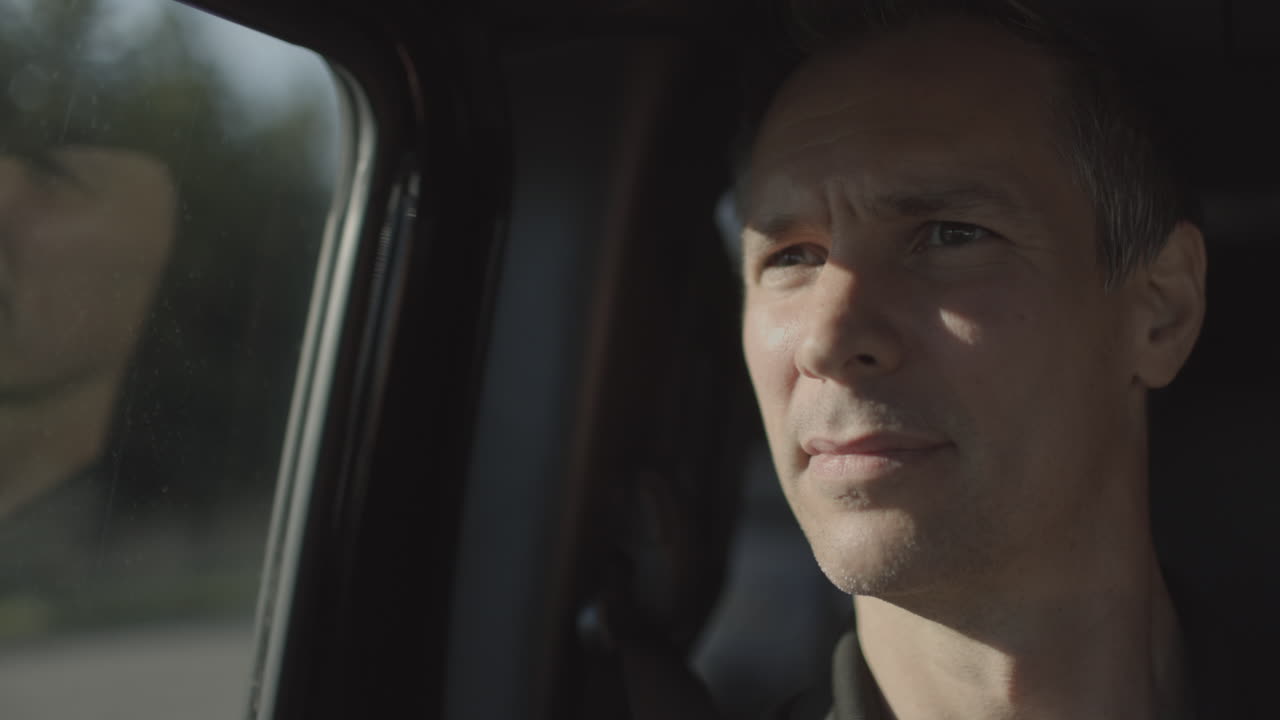 하얀 차가 지나갈 때 황금시간대에 차를 타고 있는 중년 남자의 근접 촬영