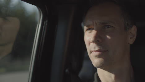 closeup of a middle aged man riding in a car during golden hour as a white car passes by