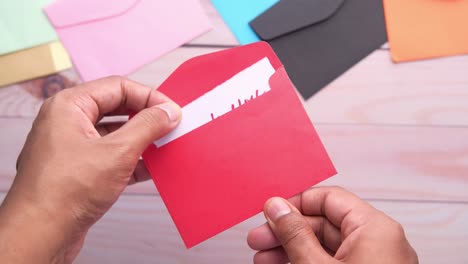manos abriendo un sobre rojo con una nota de agradecimiento
