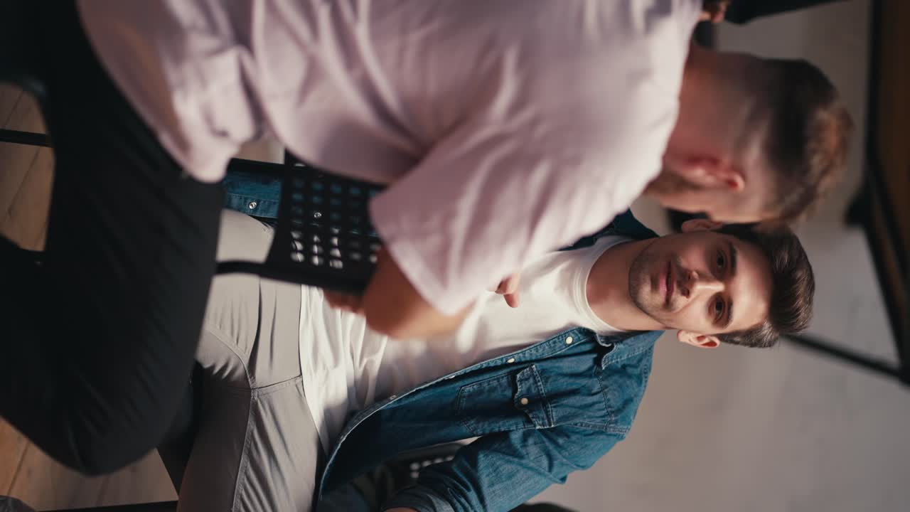 Vertical video: Two men, a brunette guy in a blue denim jacket and a man in a pink T-shirt, communicate and express their opinions during group therapy