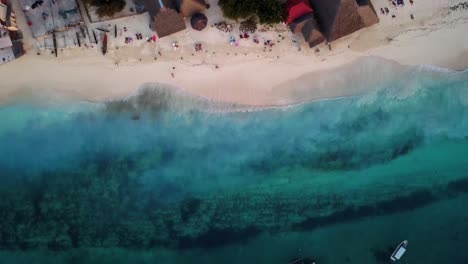 Volando-Sobre-Un-Hermoso-Océano-Azul-Y-Pequeñas-Lanchas-Con-Pequeñas-Olas-Rompiendo-Contra-Arena-Limpia-Durante-La-Puesta-De-Sol,-Playa-Nungwi,-Zanzíbar,-Isla-En-Tanzania