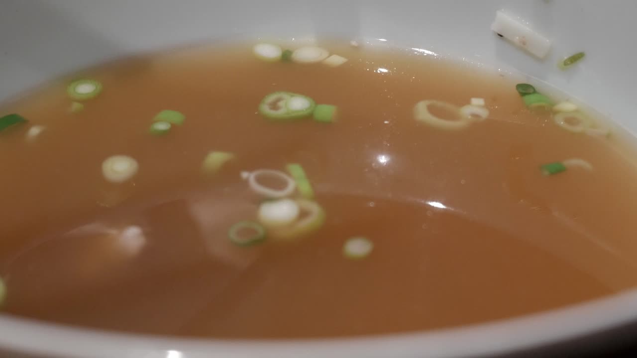 Bowl of Pho Bo soup with clear broth and fresh green onions being stirred