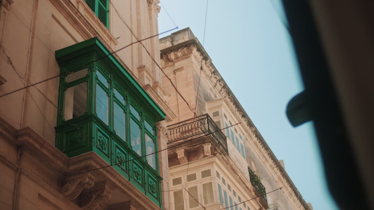 Sunlit Maltese facade with green shutters and a traditional balcony. Warm limestone architecture reflecting the island’s heritage and Mediterranean charm under clear skies