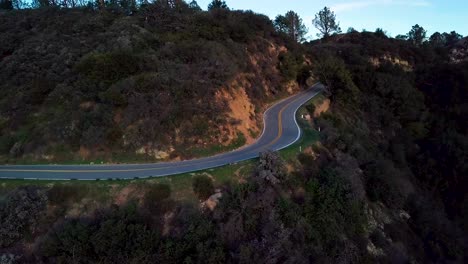 Curva-Cerrada-De-La-Carretera-De-Montaña-Al-Lado-Del-Acantilado-Empinado-Al-Amanecer,-Tobogán-De-Drones-L